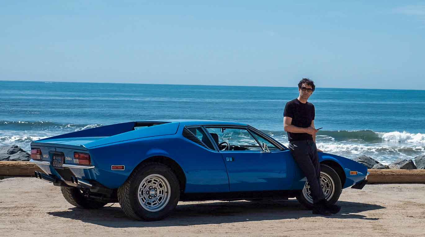 A man posing beside a blue Pantera in front of the sea